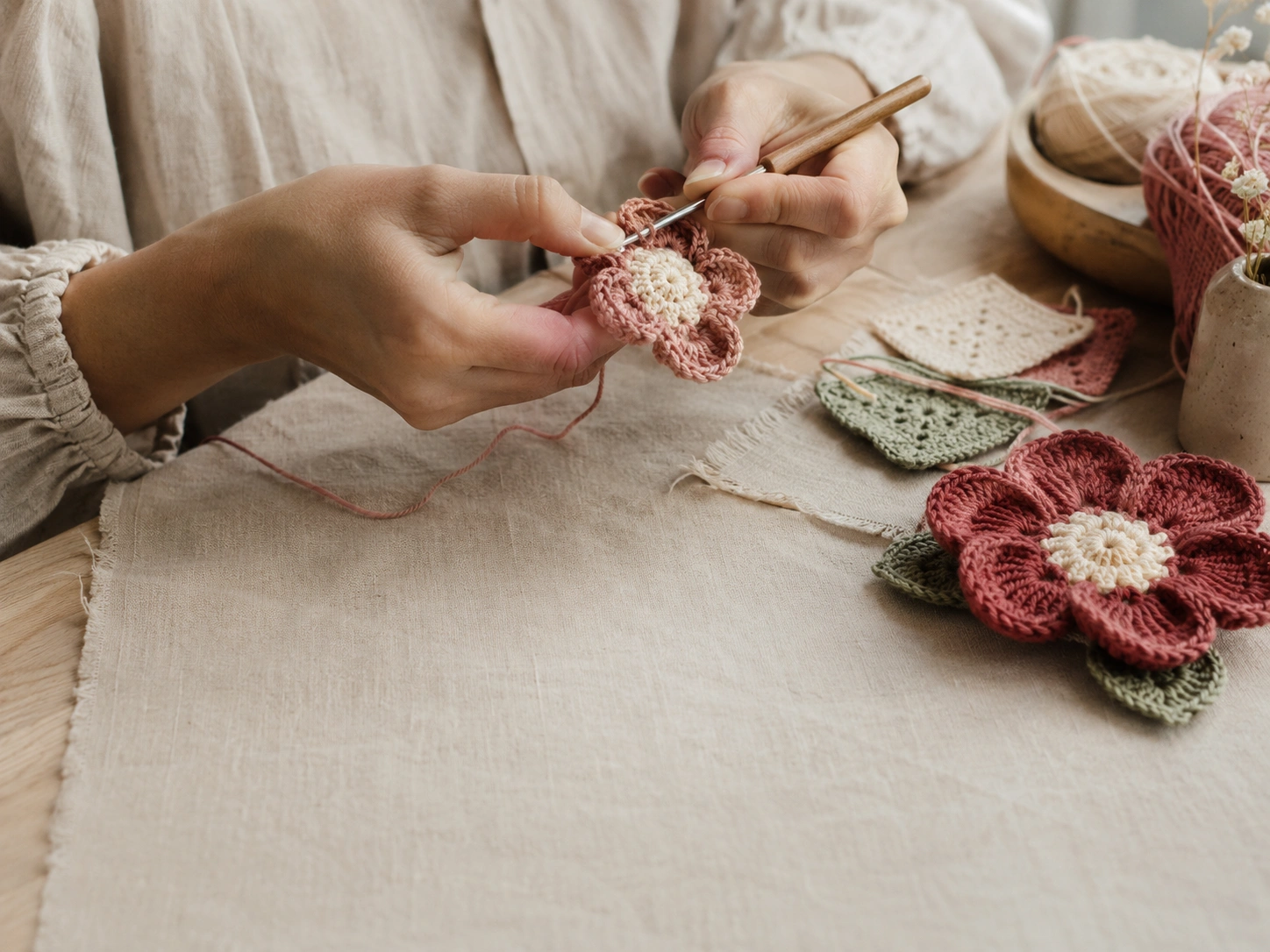 Hands carefully crafting a crochet flower on a linen-covered table