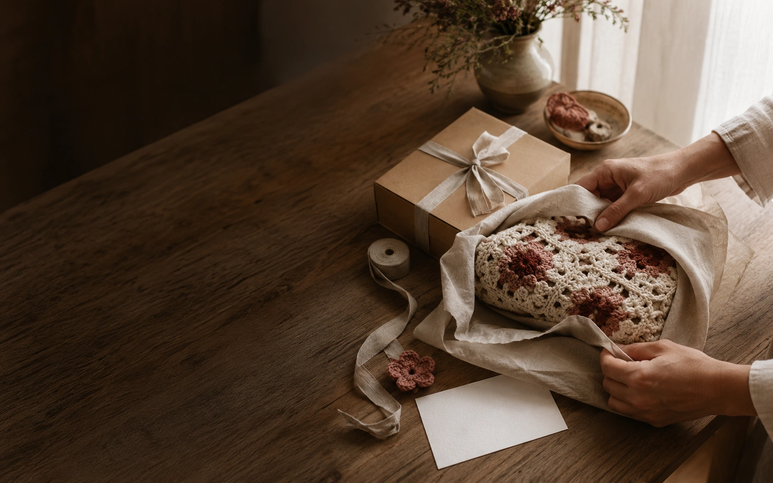 A handmade crochet gift being wrapped in linen on a warm oak table