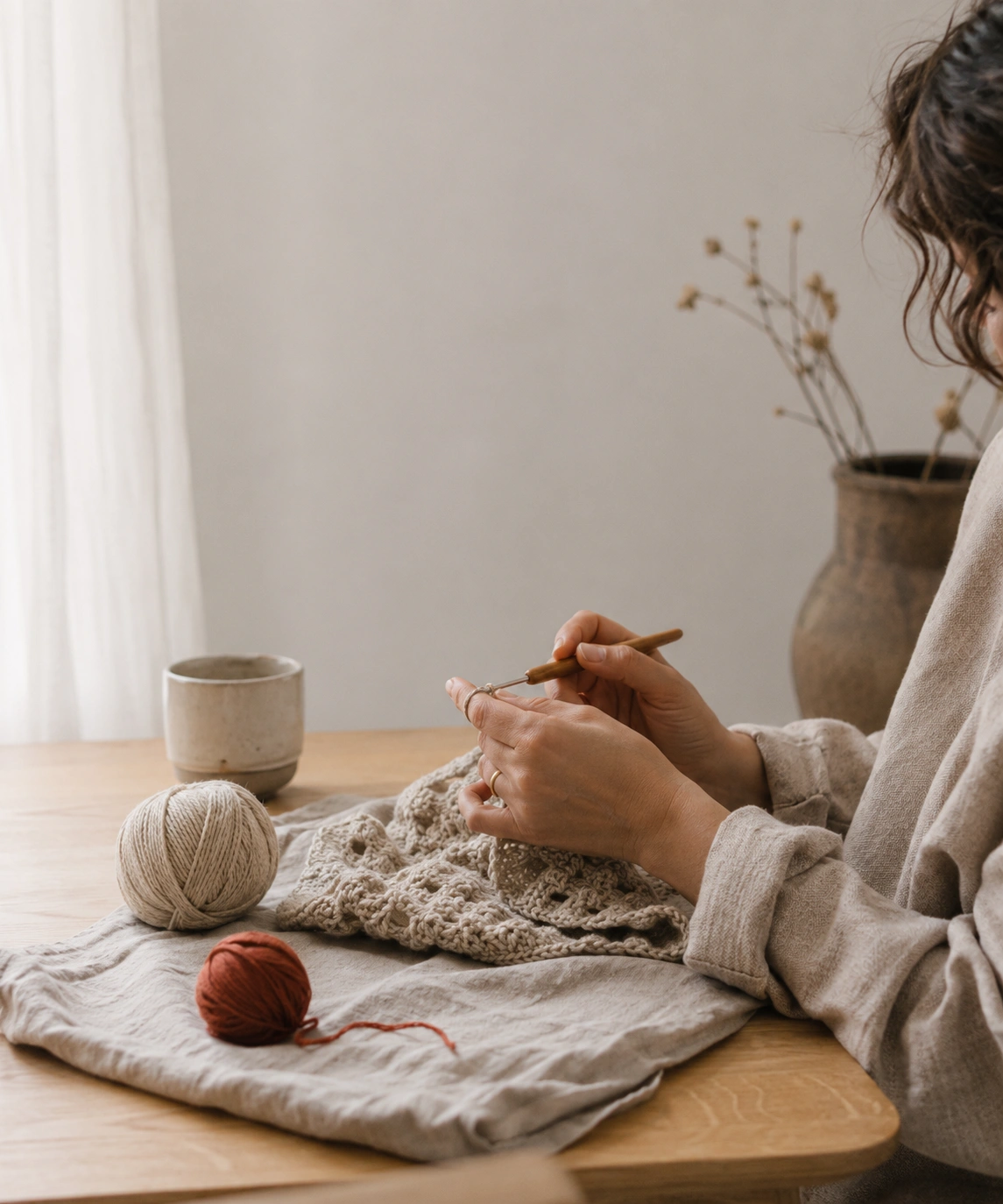 Hands carefully crocheting at an oak table in warm natural daylight