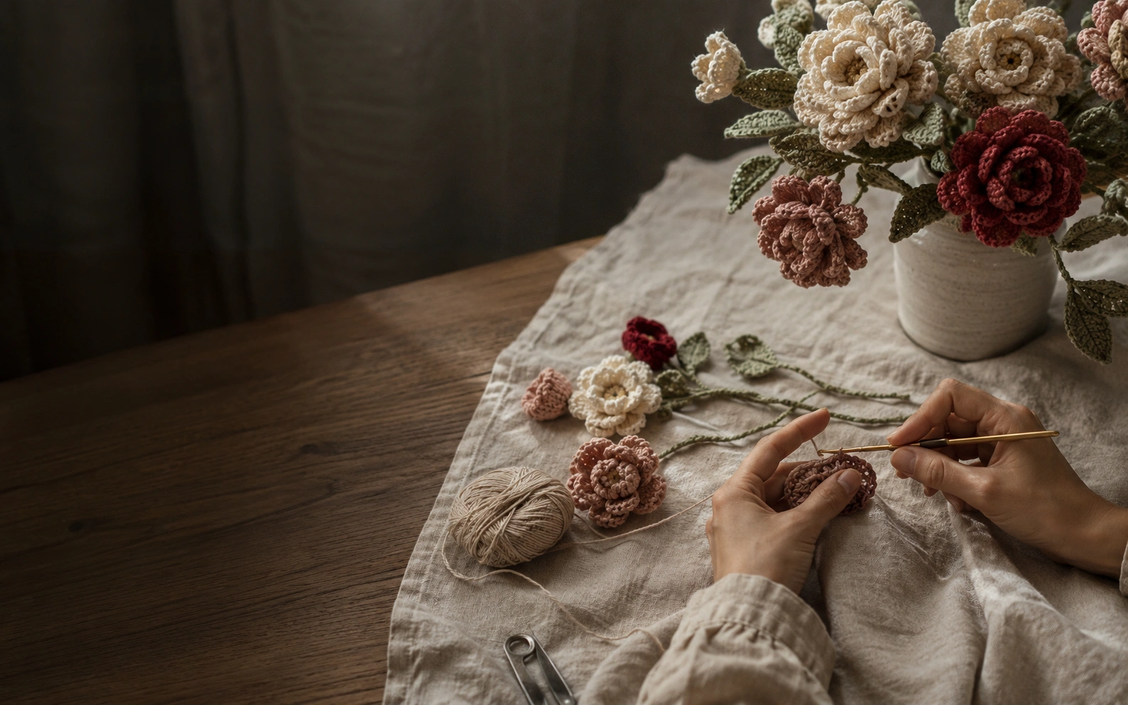 Hands crafting a handmade crochet bouquet on a warm linen table